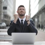 man in black suit sitting on chair beside buildings